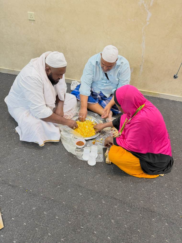 Members of the group sitting on the ground sharing a meal served from a large dish.