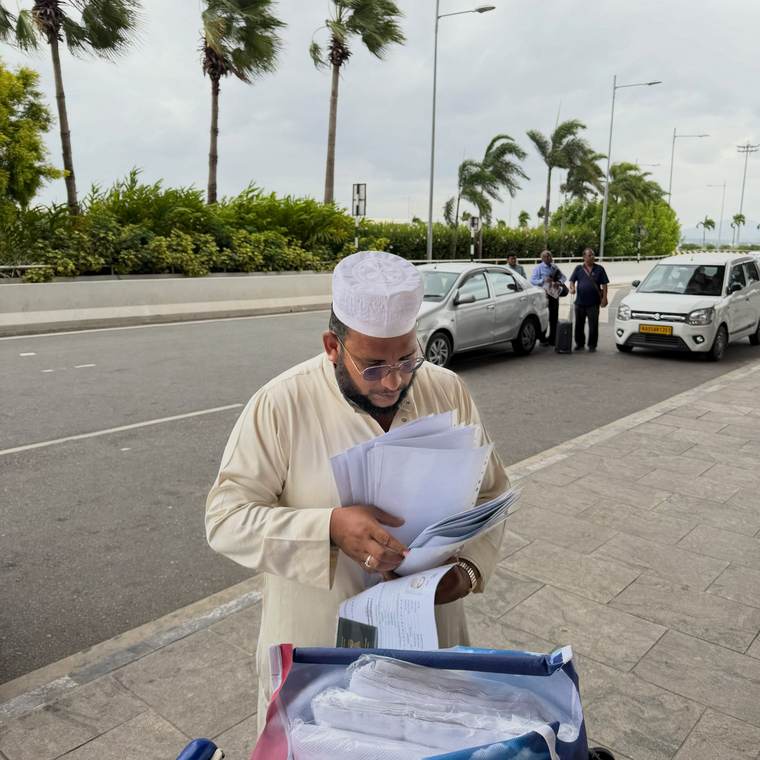 Moulavi Sadath at the kerbside outside the airport holding the group&rsquo;s travel documents.
