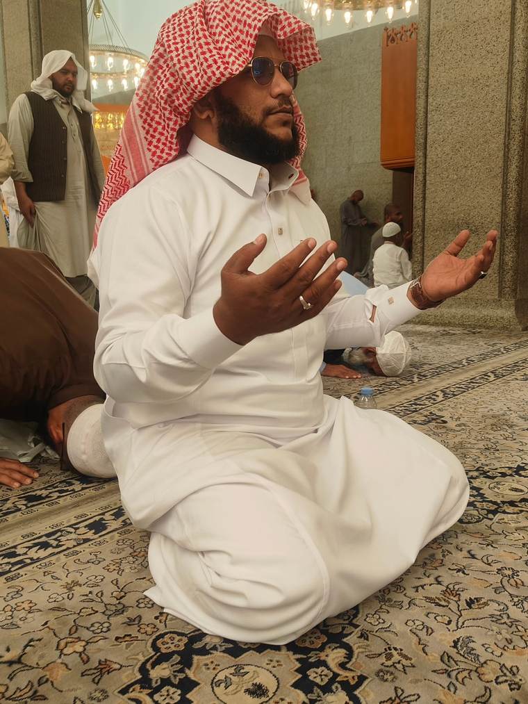 Moulavi Sadath sitting in prayer with his hands raised inside the mosque.