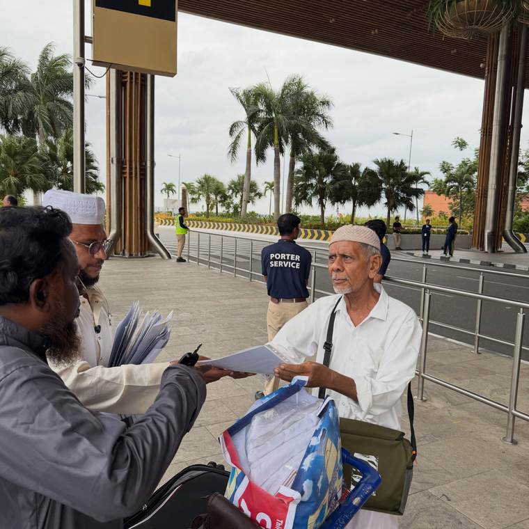 A pilgrim being handed his documents at the airport entrance, with porter service staff behind.